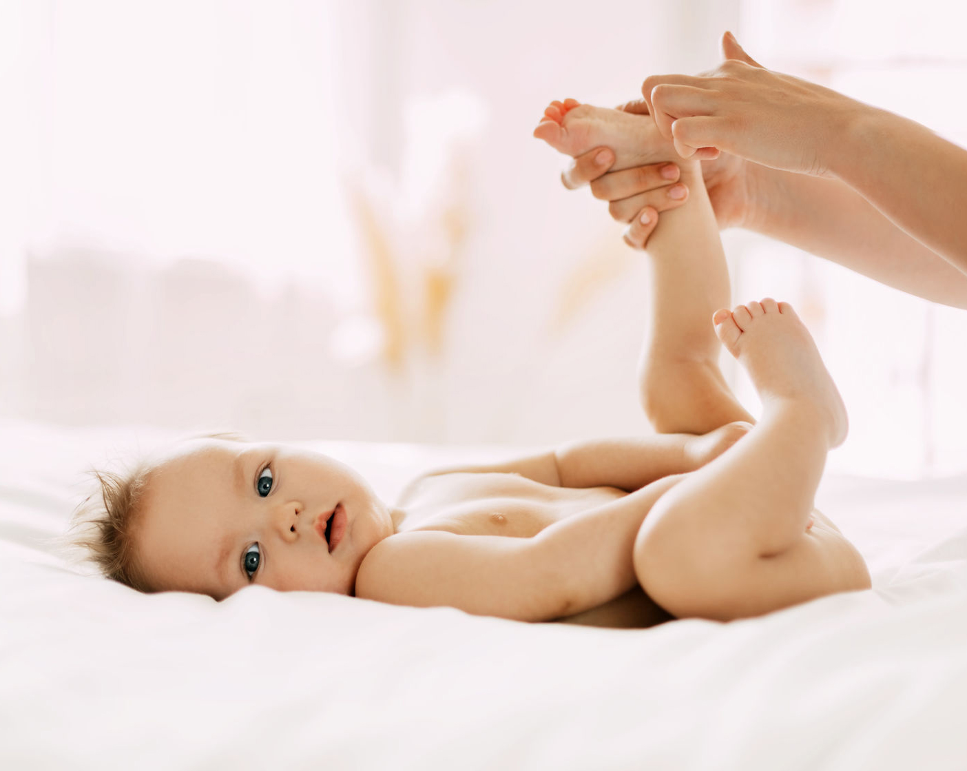 A young mother gently massages her child's legs. Child care, childhood, motherhood.